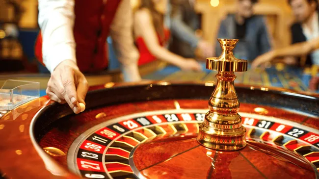 A imagem mostra um crupiê colocando uma bola na roda de uma roleta de cassino.