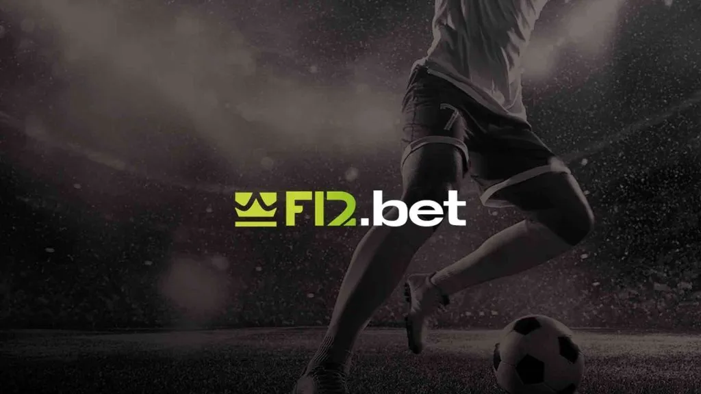 A imagem é um banner para a F12 Bet. Diz F12.bet no centro. O fundo mostra um jogador de futebol em um campo de futebol com uma bola. A foto é tirada da cintura para baixo e está em preto e branco.