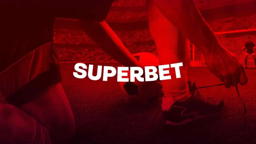 A imagem é um banner para a Superbet. Diz Superbet ao longo do meio e o fundo tem a imagem de um homem amarrando os cadarços no meio de um campo de futebol ao lado de uma bola, com um filtro vermelho.