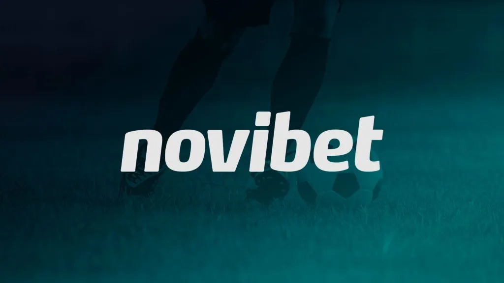 A imagem é um banner para a Novibet; ela mostra um jogador de futebol prestes a chutar uma bola. A imagem é dos joelhos para baixo e tem um filtro azul.