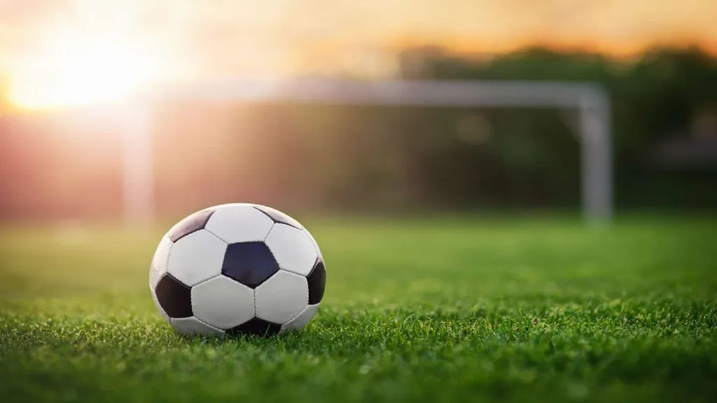 A imagem mostra uma típica bola de futebol preta e branca na posição de pênalti, como se alguém estivesse prestes a chutar para o gol.