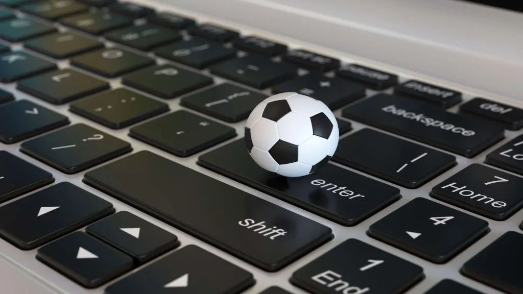 A imagem mostra uma bolinha de futebol acima do teclado de um laptop. A bolinha de futebol cabe dentro da tecla Enter.