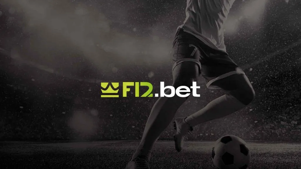 A imagem é um banner para a F12 bet. Diz F12.bet no centro. O fundo mostra um jogador de futebol em um campo de futebol com uma bola. A foto é tirada da cintura para baixo e está em preto e branco.