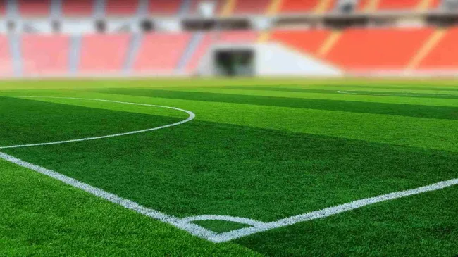A imagem mostra um campo de futebol em um estádio visto do canto. O estádio está vazio e é de dia. A imagem é uma representação de que o futebol também será jogado nas Olimpíadas 2024.