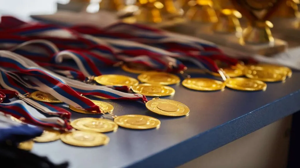 A imagem mostra uma coleção de medalhas de ouro para as Olimpíadas de 2024. Elas estão em cima de uma mesa azul.