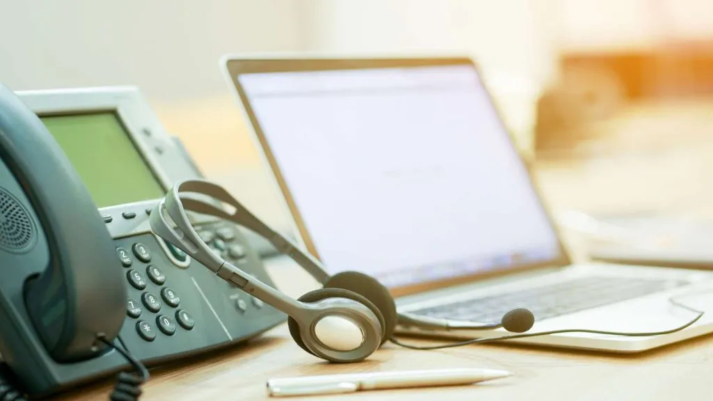 A imagem mostra um telefone fixo, um headset e um laptop. Isso representa o Serviço de Atendimento ao Cliente da Betano.