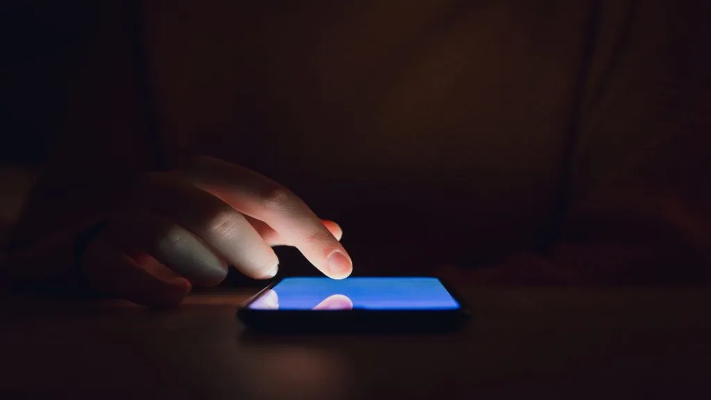 A imagem mostra uma mão usando um celular sobre uma mesa. Isso representa que os jogadores podem baixar o aplicativo da Betano e usar o código de indicação Betano.