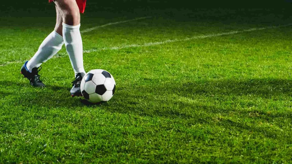 Esta imagem mostra um jogador com uma bola de futebol no campo, a foto foi tirada dos joelhos para baixo.