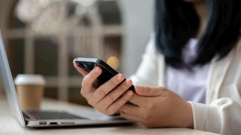 A imagem mostra uma mulher com o celular na mão, representando que a Betnacional funciona bem através do app e do site móvel.