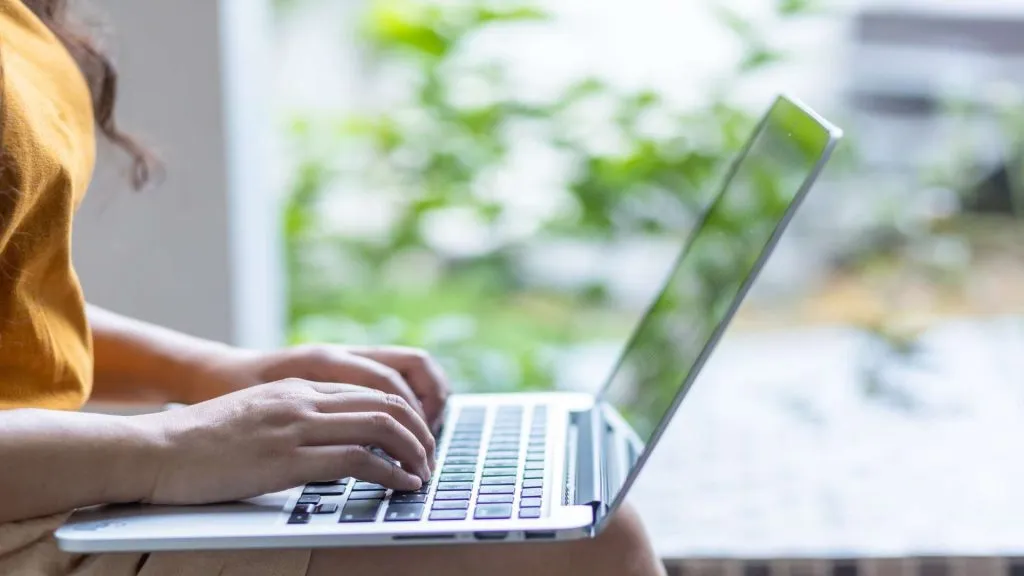 A imagem mostra uma mulher com um laptop usando o código no site da Aposta Ganha.
