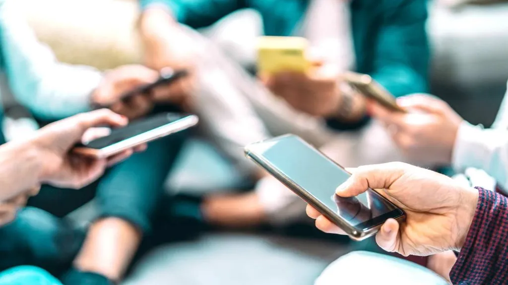 A imagem mostra cinco pessoas segurando um celular cada uma. Isso demonstra como você pode apostar na Sportingbet app ou pelo site web.