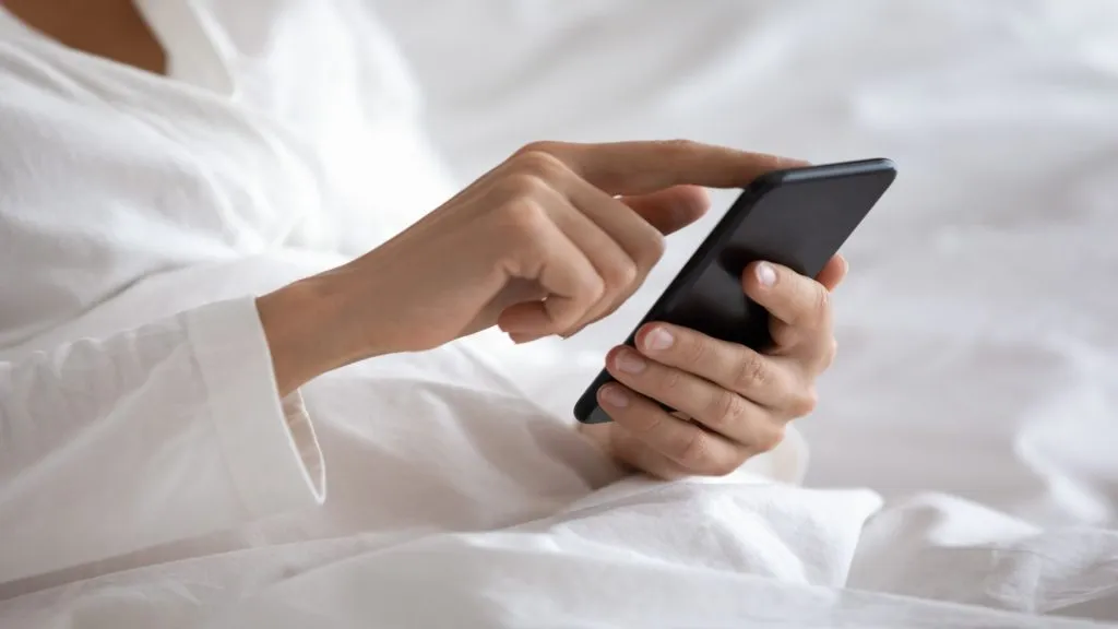 A imagem mostra uma mulher usando o aplicativo da Sportingbet em seu celular enquanto está na cama.