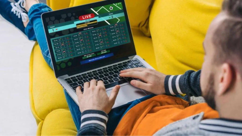 A imagem é de um homem sentado em um sofá com um laptop no colo, usando o código promocional EsportivaVIP para apostas ao vivo.