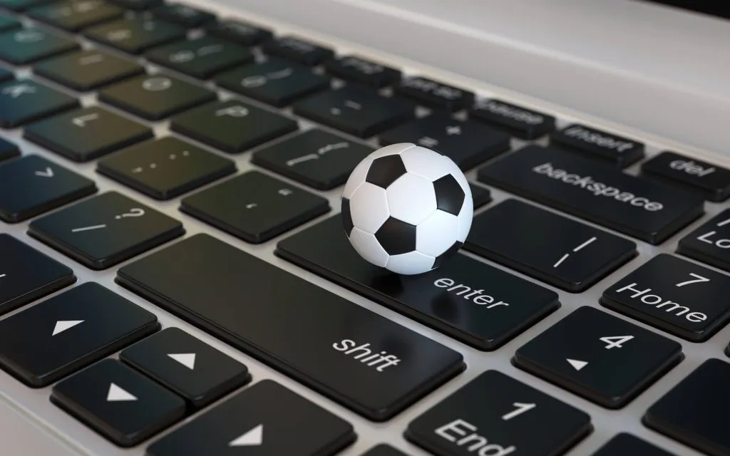 A imagem mostra uma bolinha de futebol em cima do teclado de um laptop. A bolinha de futebol cabe dentro da tecla Enter.