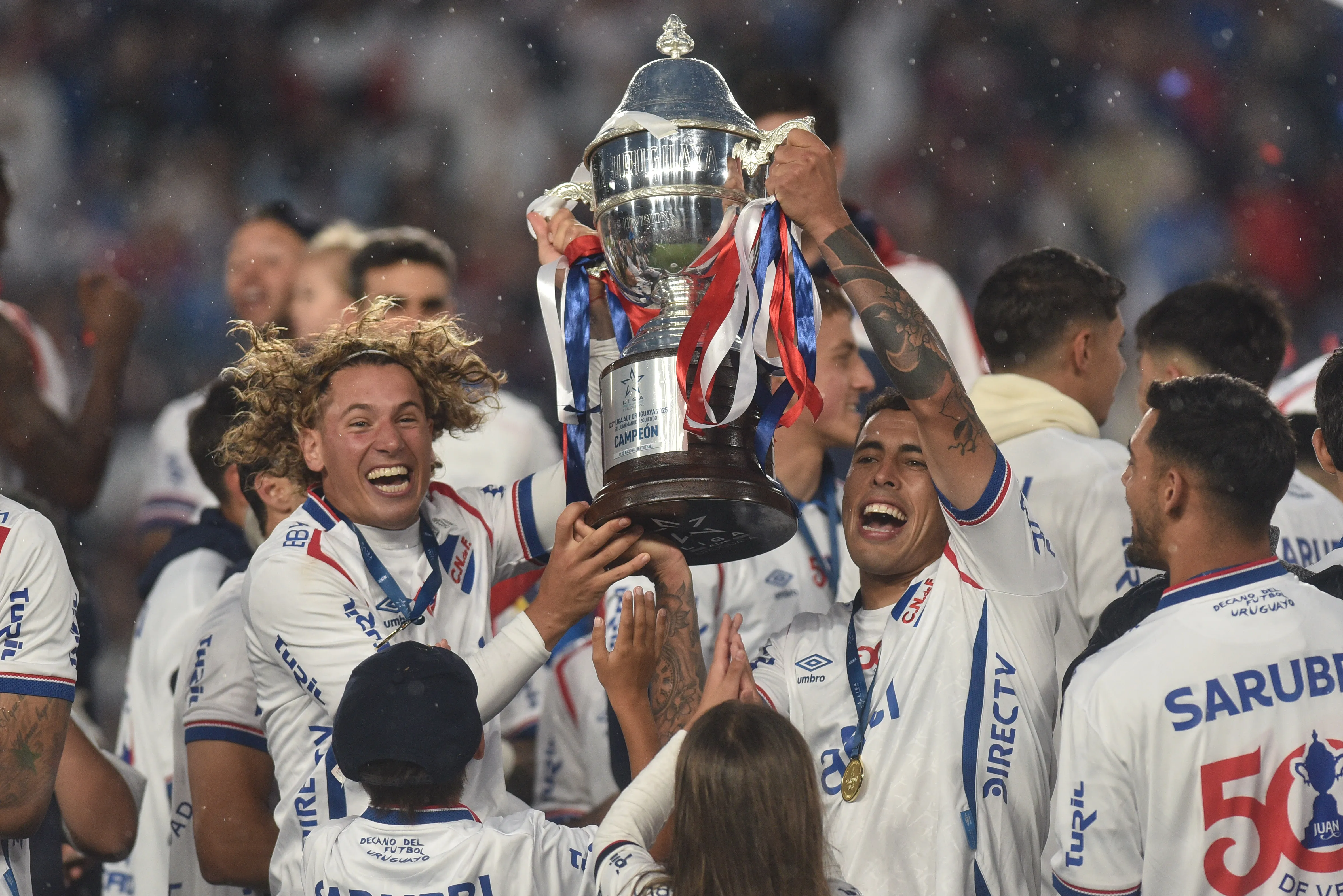 MONTEVIDEO, URUGUAY – NOVEMBER 30: Luciano Boggio and Christian Oliva of Nacional celebrate lifting the trophy after winning the Campeonato Uruguayo 2025 second leg final match between Nacional and Peñarol at Gran Parque Central stadium on November 30, 2025 in Montevideo, Uruguay. (Photo by Guillermo Legaria/Getty Images)
