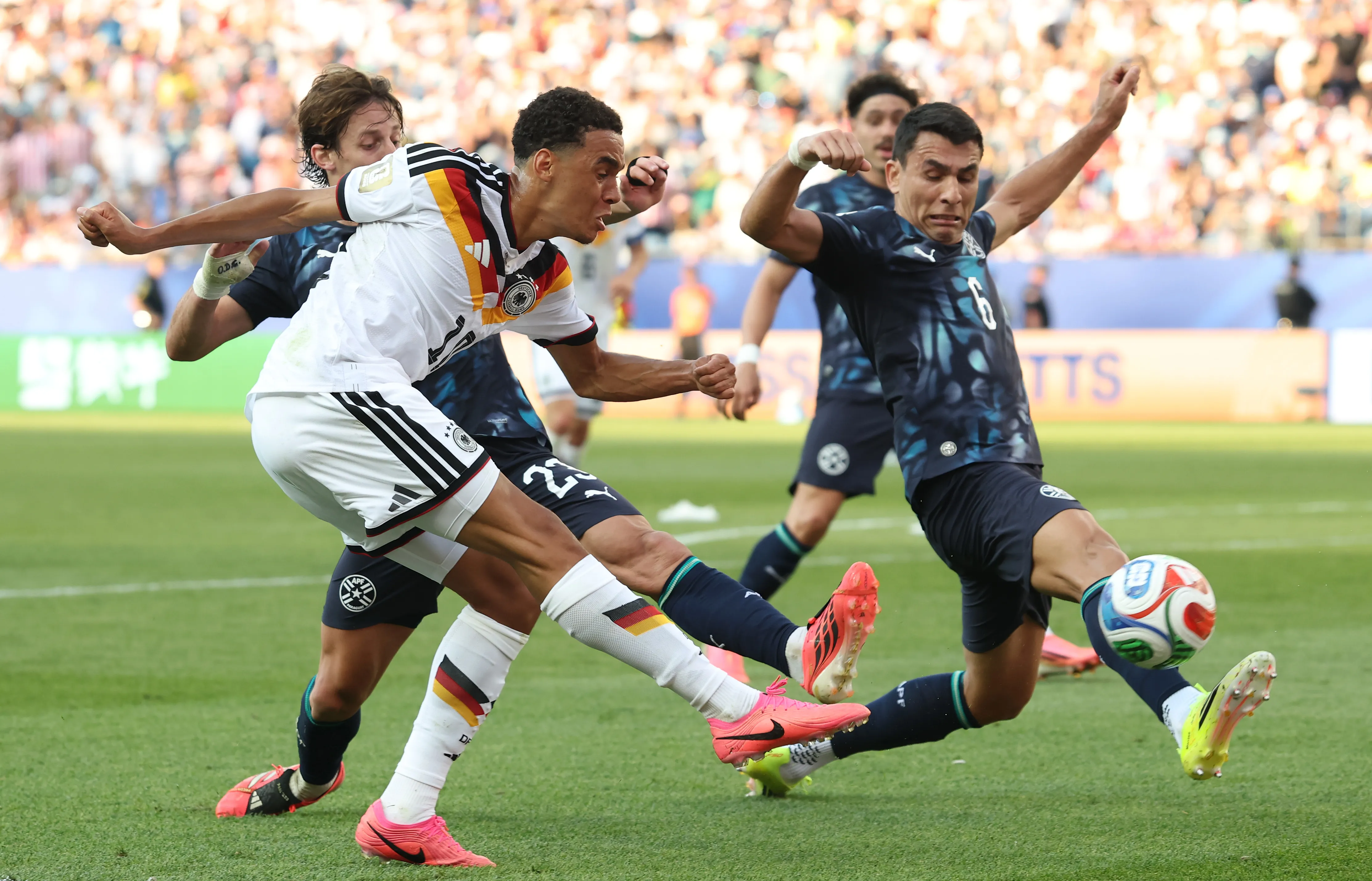 FOXBOROUGH, MASSACHUSETTS – JUNE 29: Jamal Musiala #10 of Germany crosses against Matias Galarza #23 and Junior Alonso #6 of Paraguay during the FIFA World Cup 2026 Round Of 32 match between Germany and Paraguay at Boston Stadium on June 29, 2026 in Foxborough, Massachusetts. (Photo by Alexander Hassenstein/Getty Images)